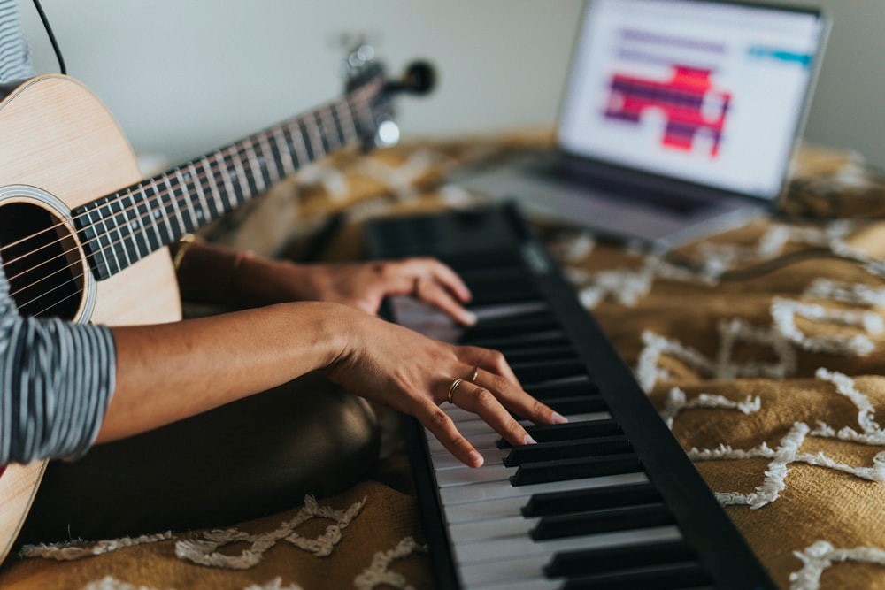 Image of hands playing a piano and a guitar in the background