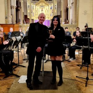 Young musician holding a trophy with a tutor at the front of a church