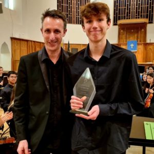 Young musician holding a trophy with a tutor at the front of a church