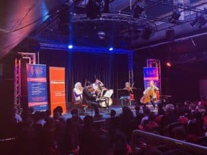 Young people are watching a string quintet performing on a stage.