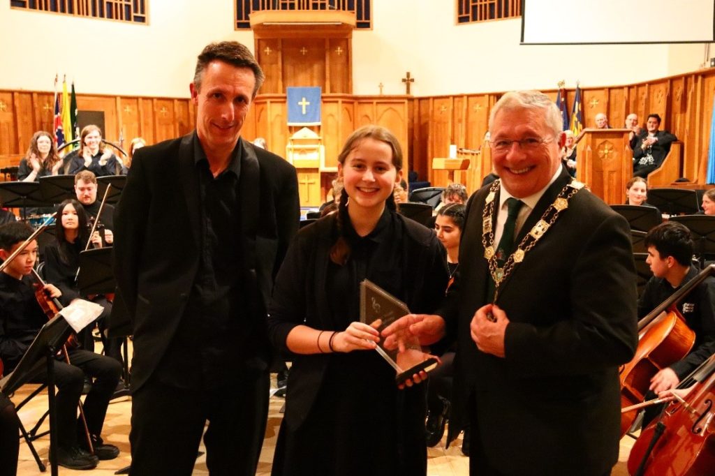 Student with conductor and deputy mayor receiving an award.