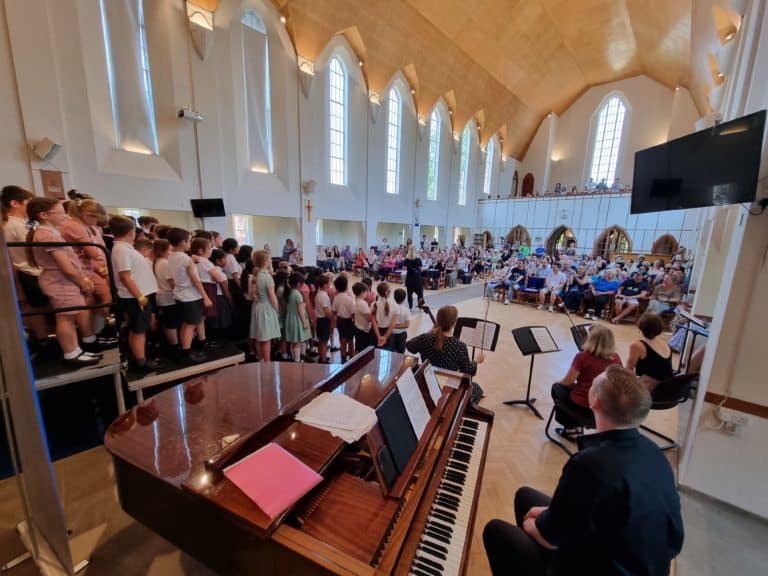 A concert in a large church with children sing on a raised platform looking at the audience.