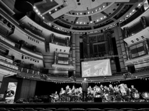 A black and white photo of a musical group performing onstage in a large venue