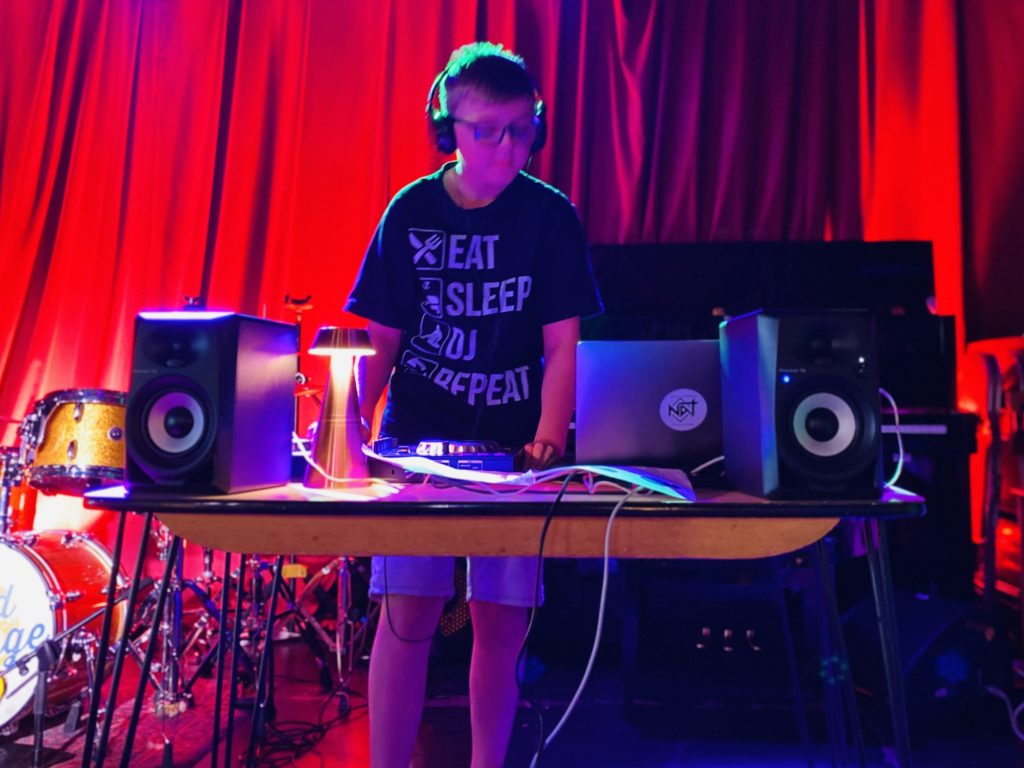 A child standing at a DJ decks with speakers and a lamp