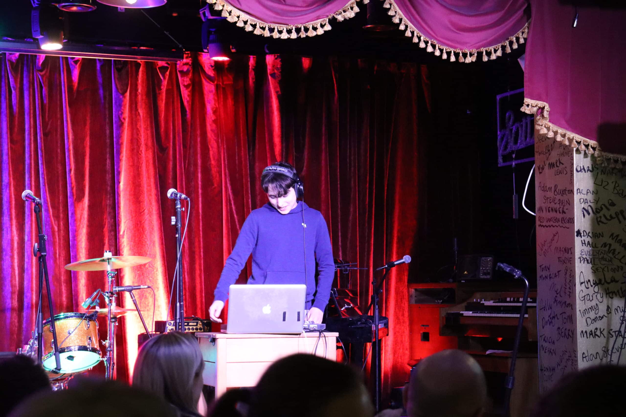 A teenager performs a DJ set with a laptop on stage