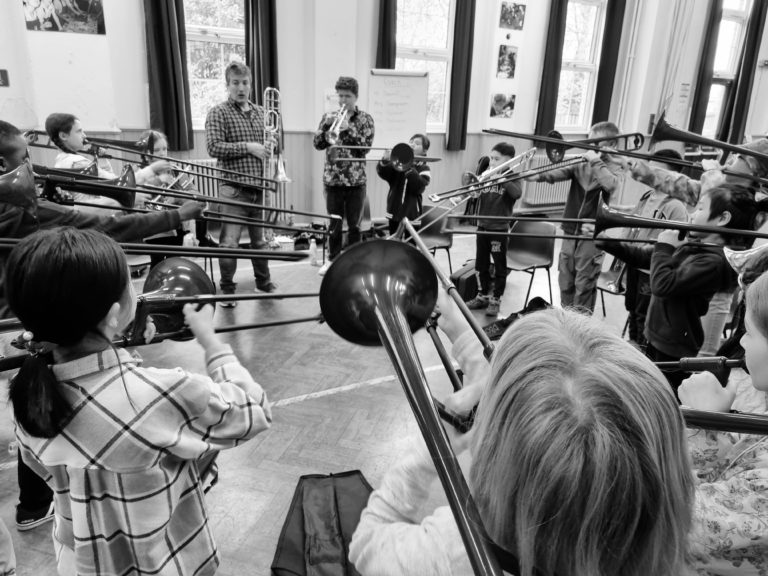 A group of students play trombones in a school hall. This is a black and white image