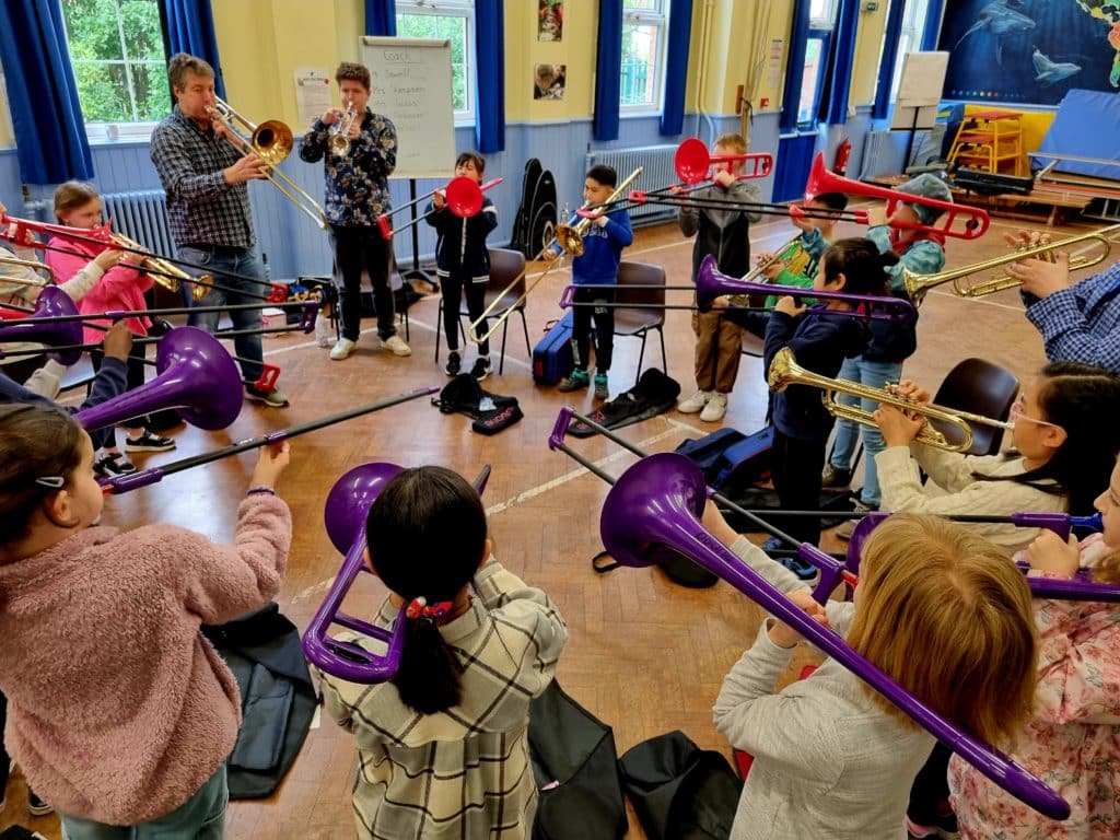 A group of young musicians play trombones and trumpets in a school hall