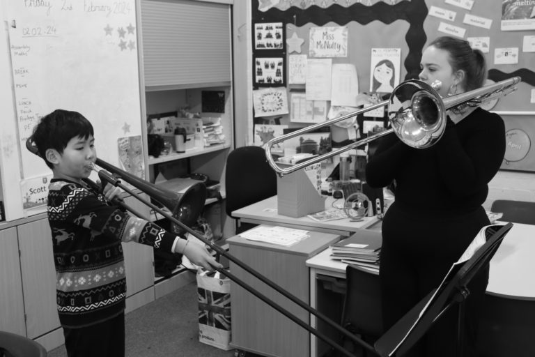 a black and white photo of a young child learning the trombone in a classroom with a teacher