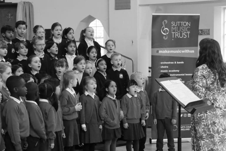 A black and white photo of a choir conductor and young children singing
