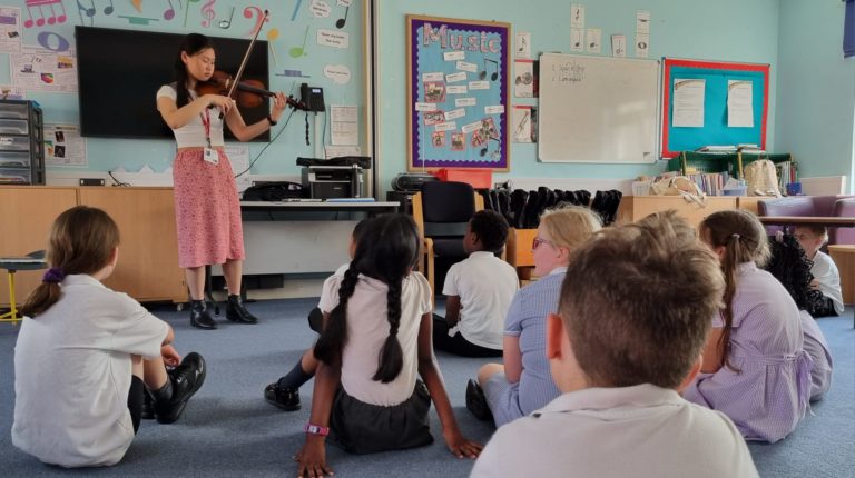 A violin player performing to a class of primary school children