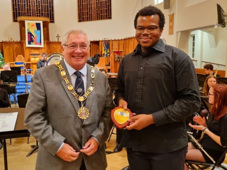 The Mayor of Sutton wearing chains and a student dressed in black. The student is holding an award plaque