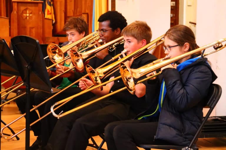 4 students playing Trombone in a church