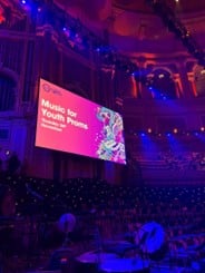 A picture of the Music for Youth logo at the Royal Albert Hall, displayed on a large screen. Pink background, music images