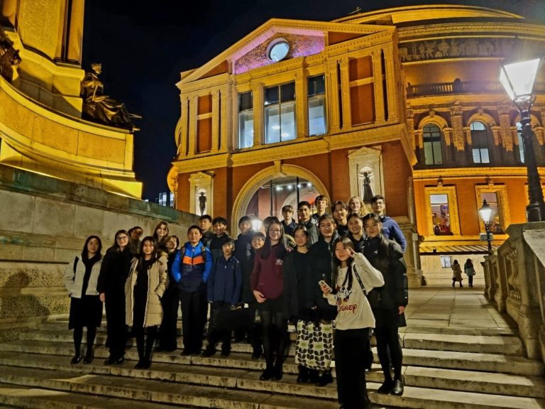 A group of students standing outside the Royal Albert Hall in the night time.