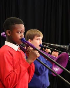 Two boys playing the trombone against a black curtain