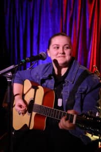 A young musician with an acoustic guitar playing on stage