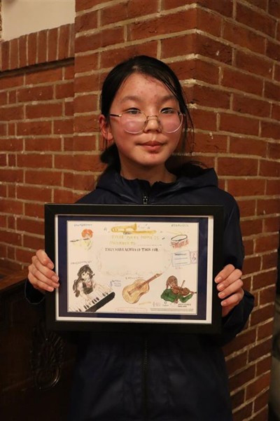 Girl standing against a brick wall with a framed copy of her winning artwork