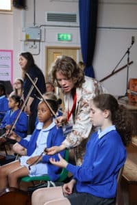 A tutor helps students with their stringed instruments in a school hall