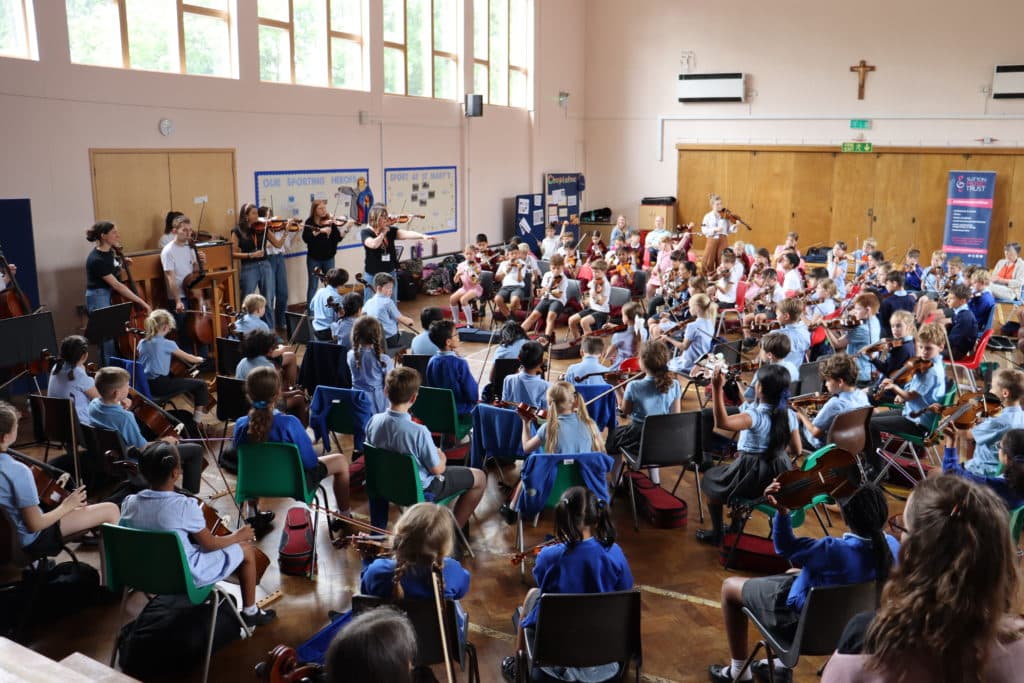 A group of students with string instruments in a school hall