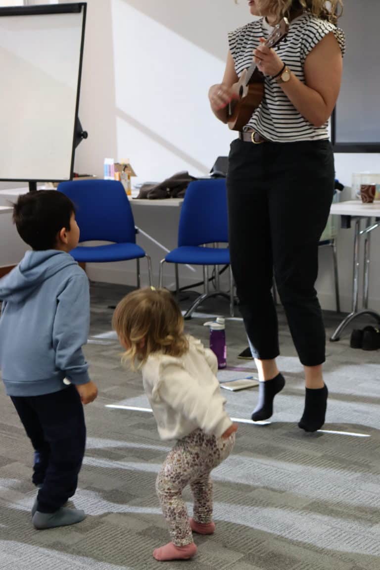 Young children jumping, an adult is playing Ukulele