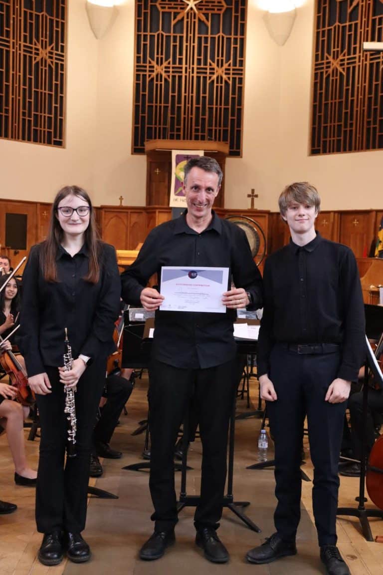 Two students pose with a conductor with a certificate