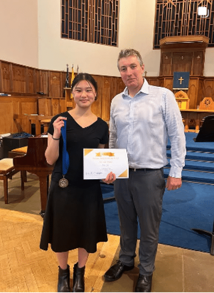 A student poses with a medal and certificate