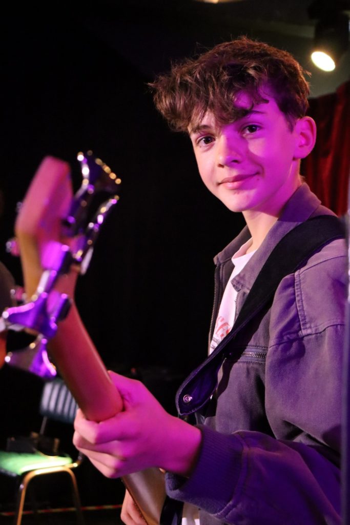 A smiling student facing the camera, playing Bass guitar