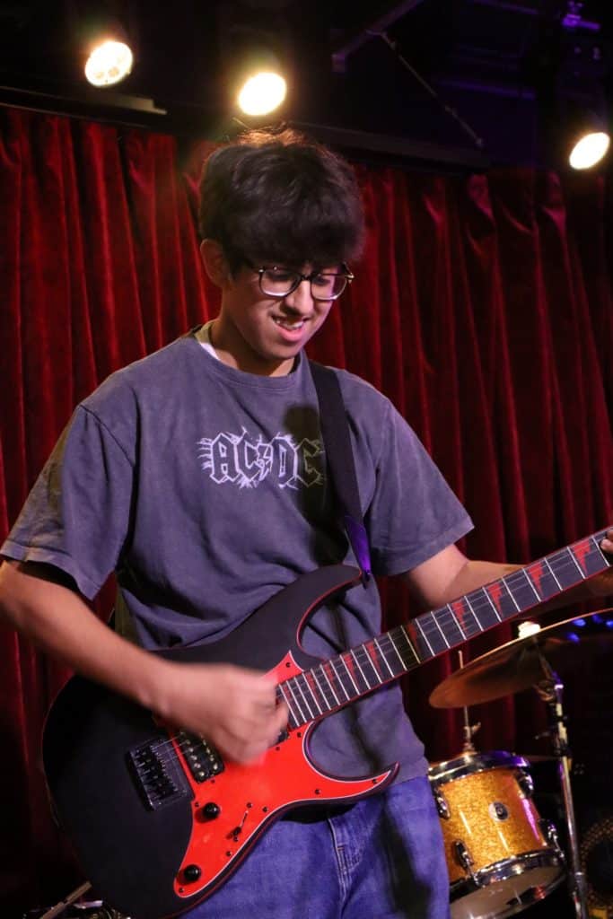 A smiling student on stage playing electric guitar