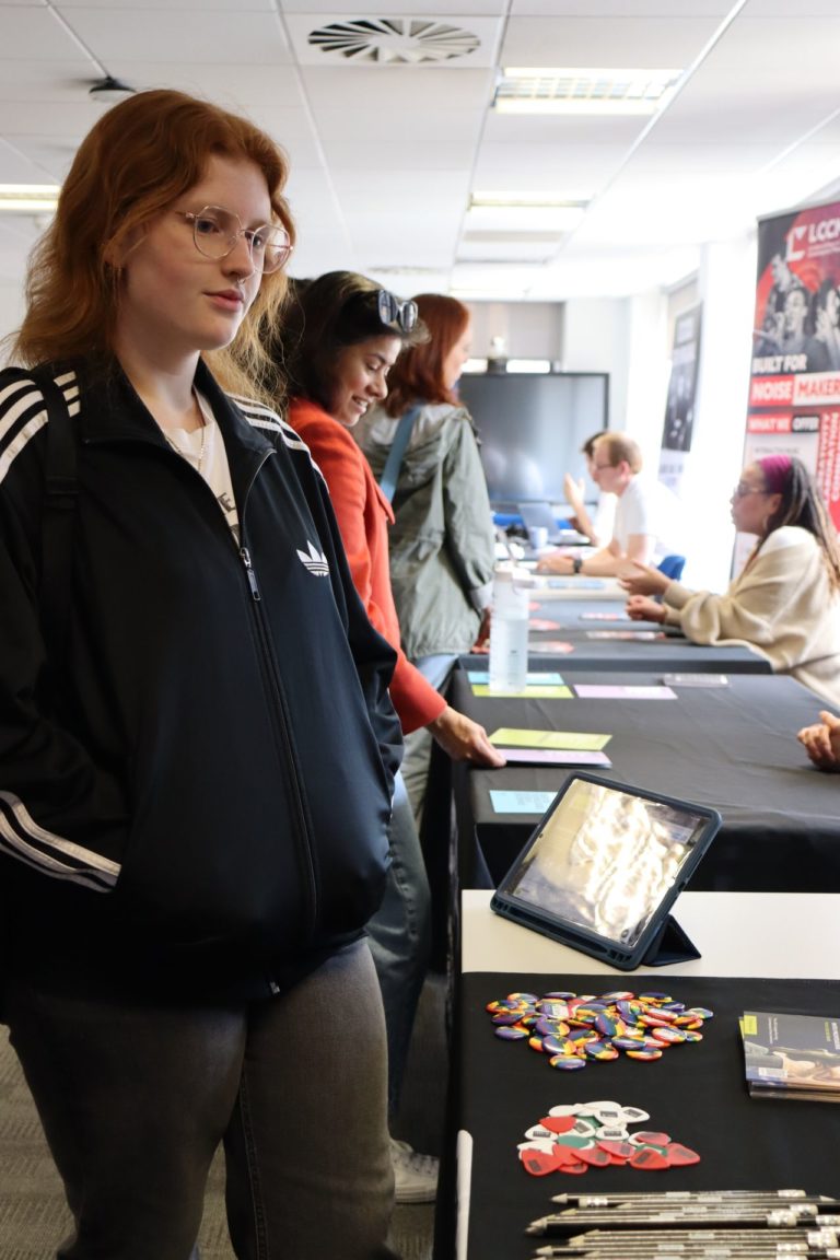 A student stands by a table with badges, flyers, and pencils on, learning more about music choices